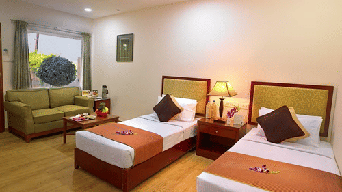 Two twin beds with a bedside lamp in between, and a sofa in the corner